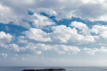 White fluffy cumulus clouds against a blue sky with haze above a body of water