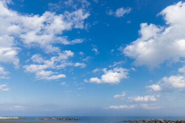 White fluffy cumulus clouds against a blue sky with haze above a body of water