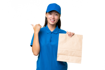 Young Asian woman taking a bag of takeaway food over isolated background pointing to the side to present a product