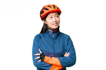 Young cyclist woman over isolated chroma key background looking up while smiling