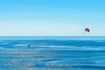 A vast expanse of the ocean gleams under the bright sky with a single Parasailing floating high...