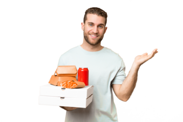 Young handsome blonde man holding pizzas and burgers over isolated background extending hands to the side for inviting to come