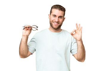 Young handsome blonde man with glasses over isolated chroma key background showing ok sign with...
