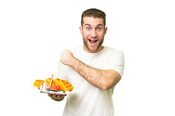 Young handsome blonde man holding waffles over isolated chroma key background celebrating a victory