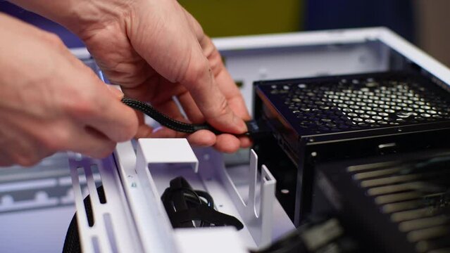Detail cropped shot of unrecognizable man plugging power cable connector from motherboard while assembling modern gaming computer. Stages of upgrading and building desktop PC Shooting in slow motion.
