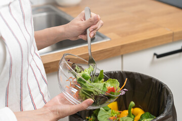 Compost from leftover food asian young housekeeper woman, female hand holding salad bowl use fork scraping waste, rotten vegetable throwing away into garbage, trash or bin. Environmentally responsible
