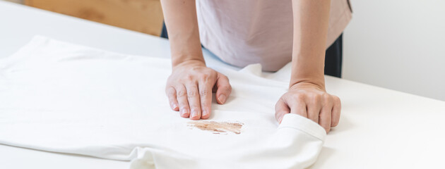 Obraz na płótnie Canvas Close up hand of housewife, maid woman holding white t-shirt, showing making cloth stain, spot dirty or smudge on clothes, dirt stains for cleaning before washing, making household working at home.