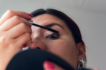 young latina woman wearing mascara with mirror in hand