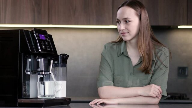 Woman using coffee machine to make to make a cappuccino at home.