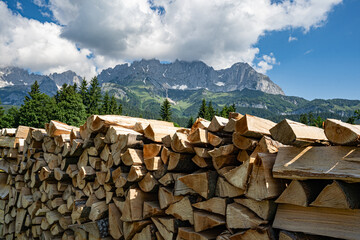 Geschichtetes Brennholz auf einer Freifläche mit den österreichischen Alpen im Hintergrund. - 784649837