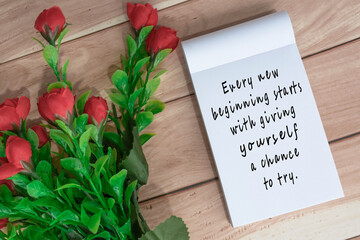 Motivational quote written on note book with artificial flowers on wooden desk