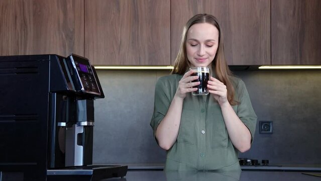 Happy woman enjoying fresh aromatic coffee near modern machine in kitchen.