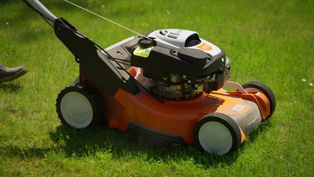 Lawnmower on Freshly Cut Grass. Vibrant orange lawnmower on a freshly mowed lawn in sunlight.