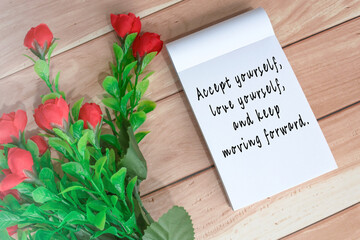 Motivational quote written on note book with artificial flowers on wooden desk