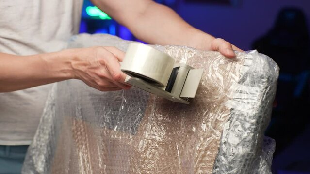Commercial moving service worker monitor and prepare to transport to new house or apartment. Closeup of unrecognizable male worker seals TV using scotch tape dispenser. Shooting in slow motion.