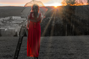 woman in a red dress and a ladder in a sunset