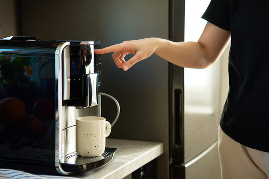 Woman preparing fresh cup of coffee with modern espresso machine. Female hand pressing button on coffee machine - Powered by Adobe