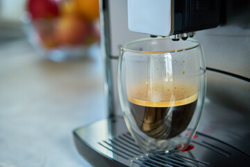 Fresh espresso at morning. Coffee machine in kitchen, close up. Modern coffee maker with freshly brewed coffee in glass cup. Kitchen appliances