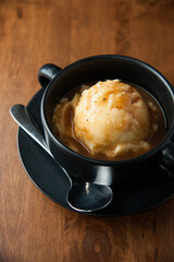Mashed potato in black cup with spoon on wooden table, vertical frame