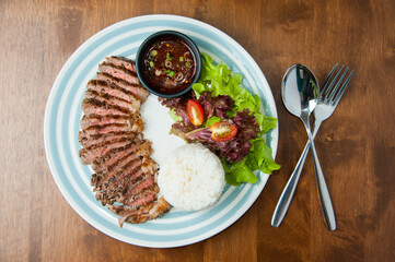Top view steak, rice and thai style sauce with spoon on wooden table