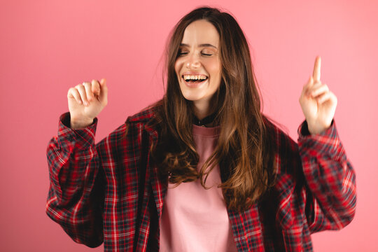 Emotions of people. Girl dancing and singing. Funny unusual brunette woman hair having fun, chill, grimaces, smiling, dancing in studio against pink background. Music, dance concept.