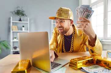 Contented rich man celebrating financial success or win, sitting at a table with gold bars, cash in...