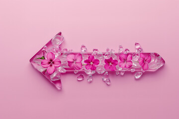 Creative an arrow pointing to the left which is made of ice with fresh spring flowers inside on pink background. Minimal pink spring concept with copy space.