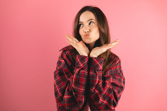 Positive millennial caucasian brunette woman making blowing kiss, isolated on pink background, studio. Love, flirt, beauty care, holiday, lifestyle, ad and offer, good news and romance, look at side.
