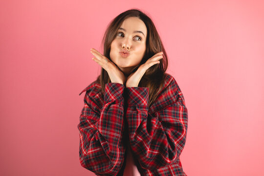 Positive millennial caucasian brunette woman making blowing kiss, isolated on pink background, studio. Love, flirt, beauty care, holiday, lifestyle, ad and offer, good news and romance, look at side.