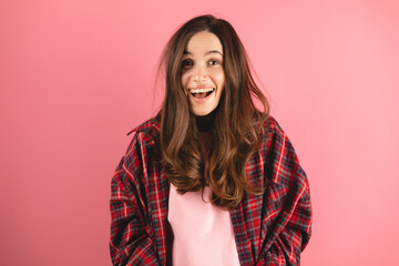 Happy cheerful young woman wearing plaid shirt rejoicing at positive news or birthday gift, looking at camera with joyful and charming smile. Brunette student girl relaxing isolated pink background.