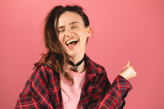 Brunette woman with high ponytail wearing pink pullover, red shirt celebrating surprised and amazed for success with arms raised, winner concept. Girl get happy, enjoy life isolated on pink background