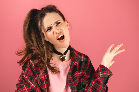 Angry unhappy young woman with high ponytail with arms out asking what's the problem who cares so what or I don't know isolated on pink background. Negative human emotions facial expression.