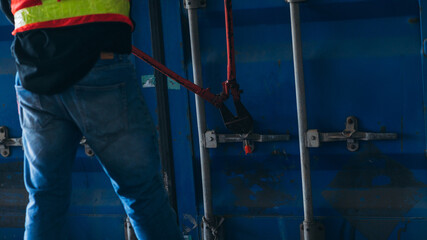 A man in a safety vest is holding a red tool in front of a blue container