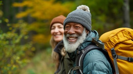 Joyful black elderly man and caucasian woman in warm hiking gear smiling in a colorful autumnal forest