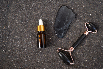 gua sha, face massage roller made of natural stone over black sand background