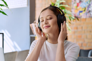 Young happy woman in headphones with closed eyes enjoying music, audio book