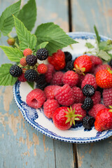 Raspberries, strawberry and wild blackberries on a vintage plate