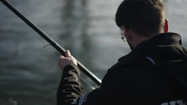 A bespectacled fisherman manipulates the bait on his rod