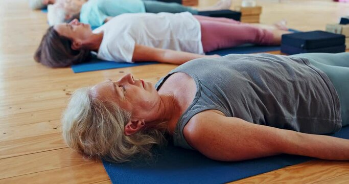 Meditation, yoga and group of women in corpse pose at gym to relax for peace, mindfulness or rest for health. Zen, calm and mature people in savasana body exercise on floor for fitness or wellness