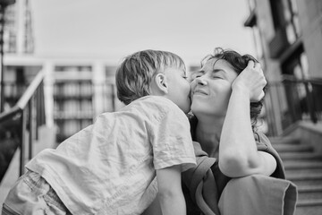 Happy family: mother and child son hugging and laugh sitting on the city stairs. motherhood...