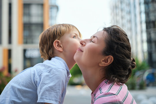 Adorable mother and son smiling happy having fun at city background. Motherhood concept, hugging. Boy 8 years old with mother in bright clothes enjoying summer day. High quality photo
