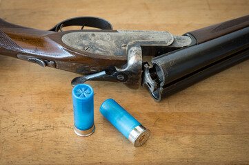 Detail of a nice old open parallel shotgun with some 12 gauge cartridges on a wooden table