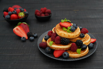 Front capture of golden pancakes on a black wooden background,  topped with fresh berries create a cozy and indulgent scene.