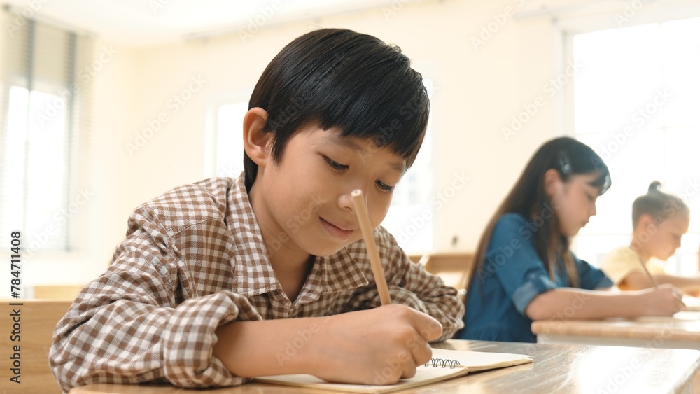 Poster close up of skilled asian student writing or taking a note during test. elementary student working o
