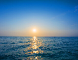 Obraz premium The sun is setting low over the ocean, casting a warm golden light across the water and creating a stunning reflection