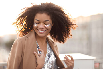 Close up outdoor portrait of happy joyful african american woman with silver shiny glitter on face...