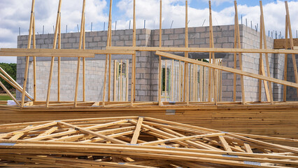 Prefabricated wooden roof trusses stacked near the concrete shell of a single-family house under construction in a suburban residential development in southwest Florida