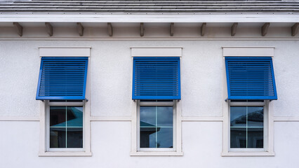 Closeup of three identical blue hurricane shutters on top halves of windows along exterior wall of an upscale single-family house under construction in a suburban development in southwest Florida