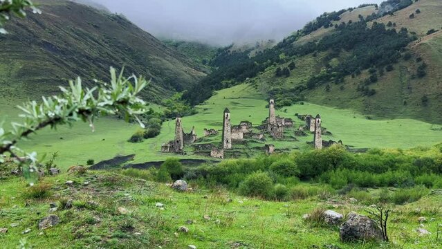 View of the medieval Targim tower complex in the Caucasus mountains surrounded by greenery. The Caucasus Mountains on a cloudy day in Ingushetia. Russia, 4K.