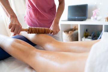 Crop masseuse doing wood therapy massage to leg of client - 784714256